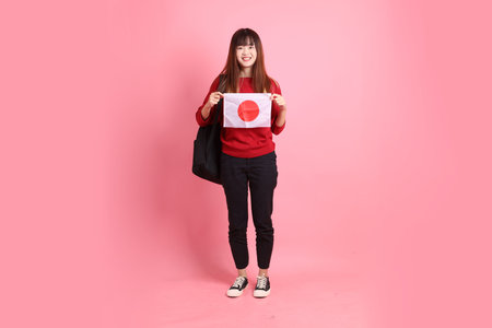 Asian college female student in red t-shirt or casual clothes carry school bag with gesture of holding flag isolated on pink background. Gen Zの写真素材