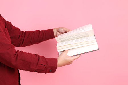 asian senior man in formal and casual red shirts with gesture of hand holding a book isolated on pink background.の写真素材
