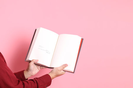 asian senior man in formal and casual red shirts with gesture of hand holding a book isolated on pink background.の写真素材