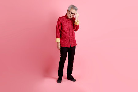 Happy Chinese new year. Asian Chinese senior man wearing red traditional cheongsam qipao or changshan dress with gesture of Headache or stress isolated on pink background.の写真素材