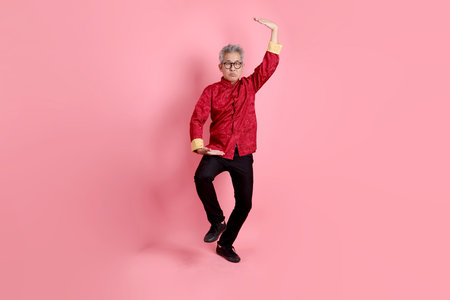 Happy Chinese new year. Asian Chinese senior man wearing red traditional cheongsam qipao or changshan dress with gesture of tai chi move isolated on pink background.の写真素材