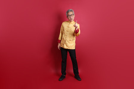 Asian Chinese senior man wearing golden traditional cheongsam qipao or changshan dress with gesture of stop, isolated on red background.の写真素材