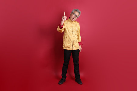 Asian Chinese senior man wearing golden traditional cheongsam qipao or changshan dress with gesture of stop, isolated on red background.の写真素材