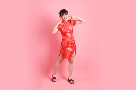 Happy Chinese new year. Asian Chinese woman wearing red traditional cheongsam qipao with gesture of Standing and smiling isolated on pink background. Gen Zの写真素材