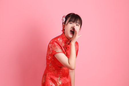 Asian Chinese woman wearing red traditional cheongsam qipao with gesture of shouting, holding megaphone isolated on pink background. Gen Zの写真素材