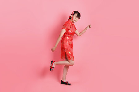 Happy Chinese new year. Asian Chinese woman wearing red traditional cheongsam qipao with gesture of walking isolated on pink background. Gen Zの写真素材