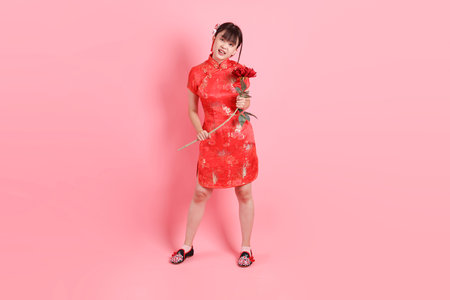 Happy Chinese new year. Asian Chinese woman wearing red traditional cheongsam qipao with gesture of Holding flower isolated on pink background. Gen Zの写真素材