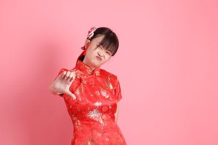 Happy Chinese new year. Asian Chinese woman wearing red traditional cheongsam qipao with gesture of thumbs down isolated on pink background. Gen Zの写真素材