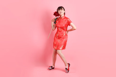 Happy Chinese new year. Asian Chinese woman wearing red traditional cheongsam qipao with gesture of Holding flower isolated on pink background. Gen Zの写真素材