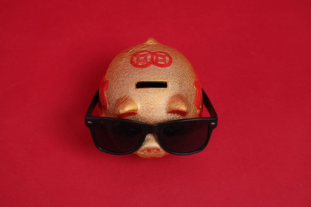 HAPPY CHINESE NEW YEAR. Golden Chinese piggy bank wearing sunglasses isolated on red background.