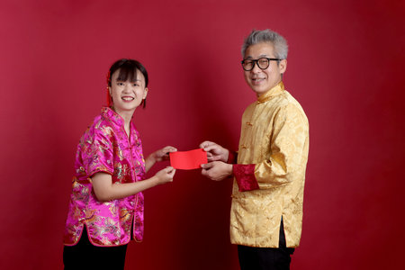 Happy Chinese new year. Asian senior man and woman wearing chinese traditional clothing with gesture of holding red envelopes isolated on pink background.の写真素材