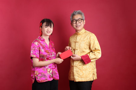 Happy Chinese new year. Asian senior man and woman wearing chinese traditional clothing with gesture of holding red envelopes isolated on pink background.の写真素材