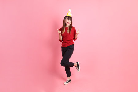 young female asian woman in red casual t-shirt with gesture of Holding birthday cake isolated on pink background. Gen Z. Heart-shaped, mini heart, love.の写真素材