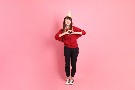 young  female asian woman in red casual t-shirt with gesture of Holding birthday cake isolated on pink background. Gen Z. Heart-shaped, mini heart, love.の写真素材
