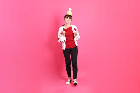 Asian woman in red t-shirt or casual clothes, red heart-shaped shirt jacket with gesture of holding birthday cake isolated on pink background. Gen Z. Heart-shaped, mini heart, love.の写真素材