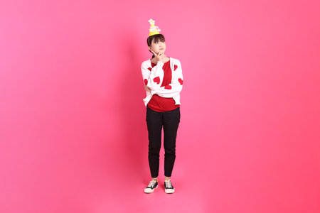 Asian woman in red t-shirt or casual clothes, red heart-shaped shirt jacket with gesture of holding birthday cake isolated on pink background. Gen Z. thinkingの写真素材