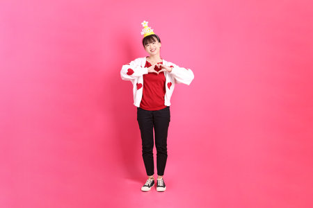 Asian woman in red t-shirt or casual clothes, red heart-shaped shirt jacket with gesture of holding birthday cake isolated on pink background. Gen Z. Heart-shaped, mini heart, love.の写真素材