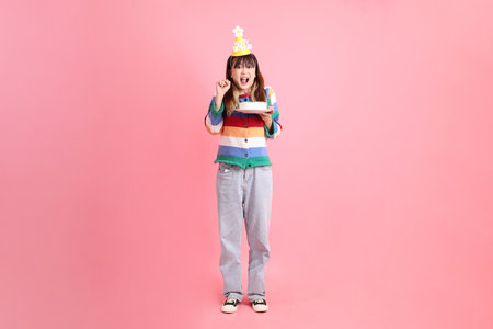 Asian woman with colorful rainbow winter clothes , casual look, birthday hat with gesture of Holding birthday cake isolated on pink background. Gen Z,の写真素材