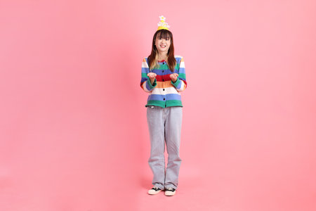 Asian woman with colorful rainbow winter clothes , casual look, birthday hat with gesture of giving and receiving isolated on pink background. Gen Z,の写真素材