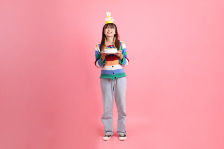 HAPPY BIRTHDAY, Asian woman with colorful rainbow winter clothes , casual look, birthday hat with gesture of Holding birthday cake isolated on pink background. Gen Z,の写真素材