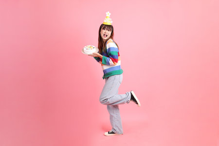 Asian woman with colorful rainbow winter clothes , casual look, birthday hat with gesture of Holding birthday cake isolated on pink background. Gen Z,の写真素材