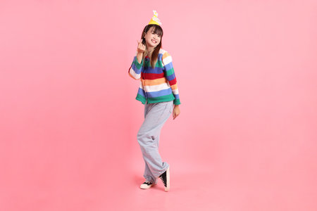 Asian woman with colorful rainbow winter clothes, casual look, birthday hat with gesture of Heart-shaped, mini heart, love isolated on pink background. Gen Z,の写真素材