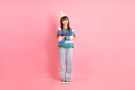 HAPPY BIRTHDAY, Asian woman with colorful rainbow winter clothes , casual look, birthday hat with gesture of Standing and smiling isolated on pink background. Gen Z,の写真素材