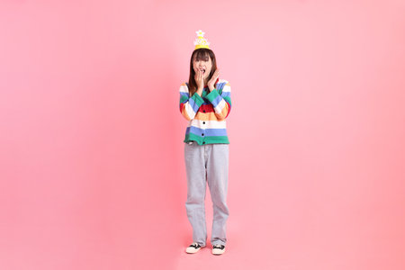 Asian woman with colorful rainbow winter clothes, casual look, birthday hat with gesture of surprise, Wow and impressive isolated on pink background. Gen Z,の写真素材