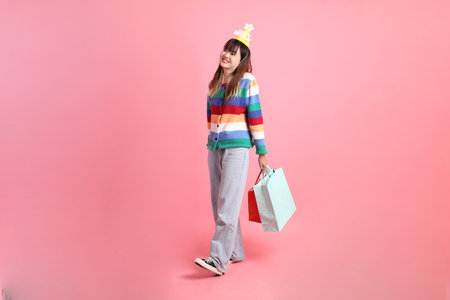 Asian woman with colorful rainbow winter clothes , casual look, birthday hat with gesture of holding shopping bag isolated on pink background. Gen Z,の写真素材