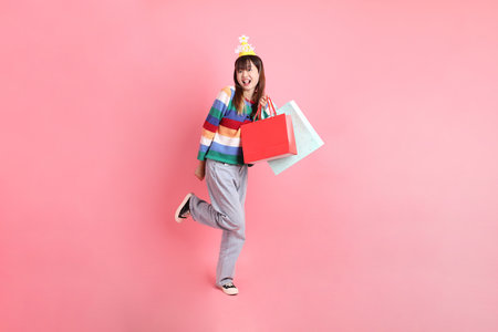 HAPPY BIRTHDAY, Asian woman with colorful rainbow winter clothes , casual look, birthday hat with gesture of holding shopping bag isolated on pink background. Gen Z,の写真素材