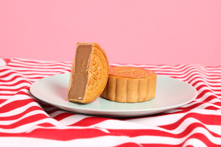 Traditional Chinese dessert Moon cake or Chinese pastry on red stripes tablecloth isolated on pink background. Chinese traditional Mid-Autumn Festival, Moon Festival.の写真素材
