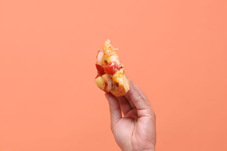 Hand holding a slice of Hawaiian pizza, a pizza topped with tomato sauce, cheese, pineapple, and ham...