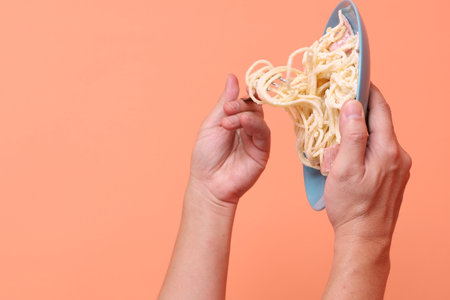 Hand holding fork eating creamy spaghetti carbonara on a green plate, isolated on an orange background. Italian food, Italian cuisine, noodles.の写真素材