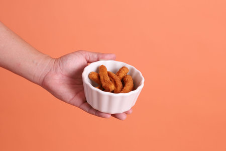 Hand holding a bowl of chicken, isolated on an orange background. Food and dining, snack, studio...