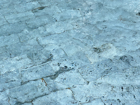 Abstract texture of stone pavement seen through rippling water. The light distortion creates a natural wave pattern on the stone surface, ideal for background, design, or artistic use.の写真素材