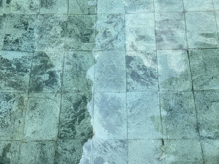 Abstract texture of stone pavement seen through rippling water. The light distortion creates a natural wave pattern on the stone surface, ideal for background, design, or artistic use.の写真素材