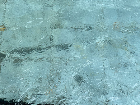 Calm and clear water surface with subtle ripples and reflections, showing faint tile patterns...
