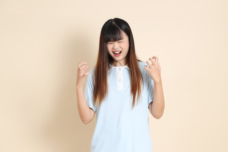 Young Asian woman wearing a light blue polo shirt, and white shorts, angry and screaming against a plain beige background. College student, Gen Z, Summerの写真素材