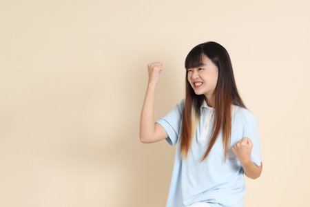 Young Asian woman wearing a light blue polo shirt, and white shorts, yes, excited, celebrating against a plain beige background. College student, Gen Z, Summerの写真素材