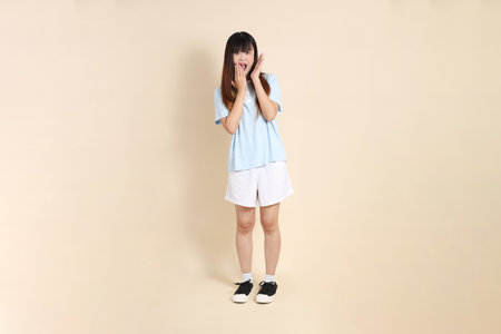 Young Asian woman wearing a light blue polo shirt, and white shorts, surprise, Wow and impressive against a plain beige background. College student, Gen Z, Summerの写真素材