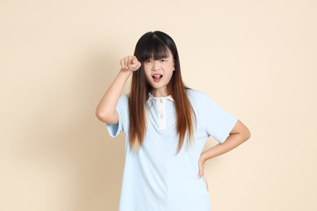Young Asian woman wearing a light blue polo shirt, and white shorts, angry and screaming against a plain beige background. College student, Gen Z, Summerの写真素材