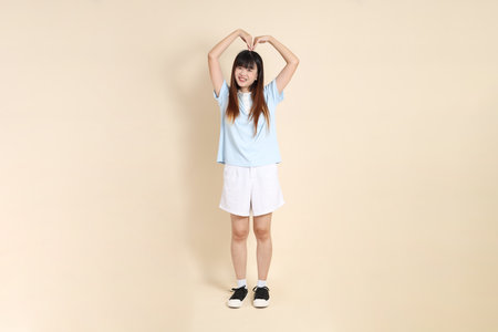 Young Asian woman wearing a light blue polo shirt, and white shorts, Heart-shaped, mini heart, love against a plain beige background. College student, Gen Z, Summerの写真素材