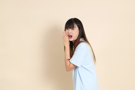 Young Asian woman wearing a light blue polo shirt, and white shorts, shouting, holding megaphone against a plain beige background. College student, Gen Z, Summerの写真素材