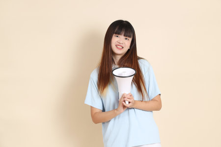 Young Asian woman wearing a light blue polo shirt, and white shorts, shouting, holding megaphone against a plain beige background. College student, Gen Z, Summerの写真素材