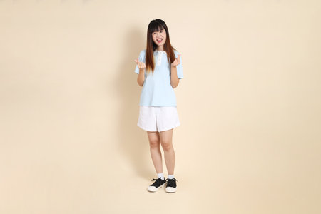 Young Asian woman wearing a light blue polo shirt, and white shorts, Heart-shaped, mini heart, love against a plain beige background. College student, Gen Z, Summerの写真素材
