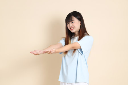 Young Asian woman wearing a light blue polo shirt, and white shorts, giving and receiving against a plain beige background. College student, Gen Z, Summerの写真素材