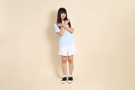 Young Asian woman wearing a light blue polo shirt, and white shorts, giving and receiving against a plain beige background. College student, Gen Z, Summerの写真素材