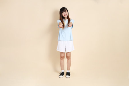 Young Asian woman wearing a light blue polo shirt, and white shorts, giving and receiving against a plain beige background. College student, Gen Z, Summerの写真素材