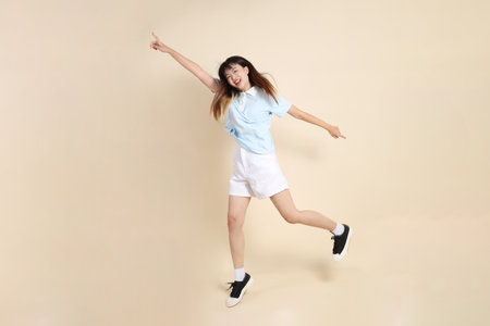 Young Asian woman wearing a light blue polo shirt, and white shorts, Jumping against a plain beige background. College student, Gen Z, Summerの写真素材