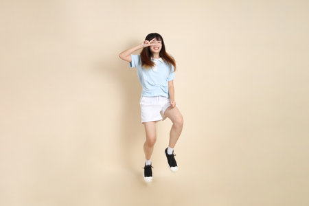 Young Asian woman wearing a light blue polo shirt, and white shorts, Jumping against a plain beige background. College student, Gen Z, Summerの写真素材